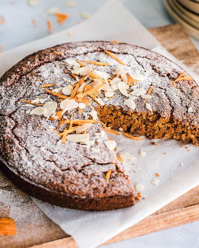 Bizcocho de almendra y naranja con láminas de almendra y ralladura sobre una tabla de madera.