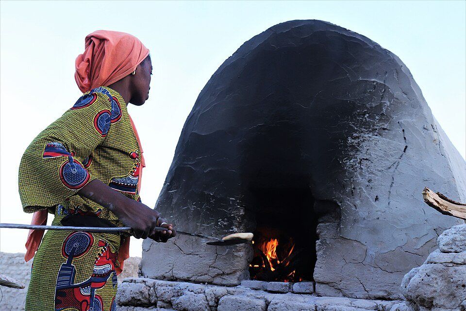 Una panadera introduce masa con una pala en un horno de barro encendido.